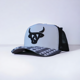 A white trucker cap with black mesh in back;  a stitched Aztec pattern on the bill and a bold black Lost Calf logo on the front